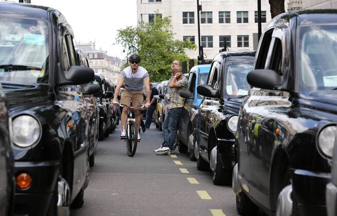 Image licensed to i-Images Picture Agency. 11 06 2014.A cyclist makes his way through lines of London black cab taxis in The Strand, as they bring central London to a halt during a demonstration against an app based service . Picture by Stephen Lock i-Images StephenxLockx xi-Images  IIM-2448-0010