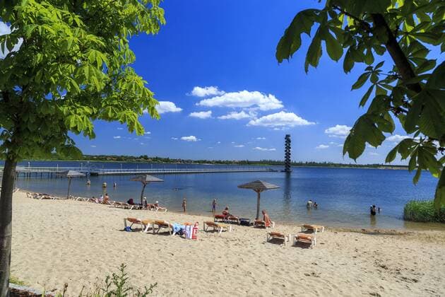 TopReiseziel Lausitzer Seenland Goitzschesee bei Bitterfeld DEU Sachsen-Anhalt Bitterfeld Â Strandbad: Der Große Goitzschesee ist der zweitgrößte See im Sächsischen Seenland. Der Tagebaurestsee gehört zum Bitterfelder Bergbaurevier. Die nordöstliche Bucht bei Mühlbeck wird Bernsteinsee genannt. 1998 wurde die Flutung des ehemaligen Tagebaugebietes mit der Einleitung von Muldewasser begonnen. Von der Lausitzer und Mitteldeutschen Bergbau-Verwaltungsgesellschaft (LMBV) wurde er bis 2006 saniert. Im Juni 2005 wurde der See für Wassersport und touristische Nutzung freigegeben. Am Stadtrand von Wolfen-Bitterfeld entstand eine weitläufige Uferzone mit Festplatz, Badestränden, einem Hafenbecken und Marina zwischen der Villa am Bernsteinsee und dem Pegelturm. Im ehemaligen mitteldeutschen Braunkohlerevier entsteht eine der größten künstlichen Seenlandschaften Deutschlands, die nach Abschuss der Flutungen 175 qk