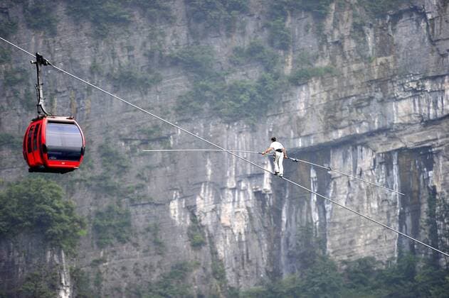 ZHANGJIAJIE, CHINA - JUNE 28: (CHINA OUT) Freddy Nock, known as Europe s King of the High Wire , walks on the Tianmen Mountain Cableway without any protective measures as a cable car goes by on June 28, 2014 in Zhangjiajie, Hunan Province of China. Freddy Nock, who is a world record holder of various events and known as Europe s King of the High Wire , once again took on the challenge of walking on Asia s longest and most dangerous cable, the Tianmen Mountain Cableway, without any protective measures. After walking 420 m, he gave up because the slope was too steep and his feet were too slippery. In 2010, Nock did the same challenge at Tianmen Mountain Cableway. He walked for about 200 m before giving up due to severe rolling and shaking of the cable beneath his feet.  CFP454399268