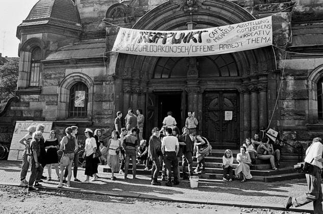 Auf hartes Drängen der SED hatte die evangelische Kirchenleitung oppositionelle Gruppen nicht zum offiziellen Programm des Leipziger Kirchentags vom 6. bis 9. Juli 1989, dem letzten evangelischen Kirchentag in der DDR, zugelassen. (Foto vom 08.07.1989: vor der Michaeliskirche in Leipzig, Treffpunkt Sozialdiakonisch Offene Arbeit , Cafe Michaelis, Ausstellung, Gottesdienst - eine Initiative parallel zum Kichentag) Sie nannten ihre Zusammenkunft deshalb Statt-Kirchentag , gingen in die Lukaskirche des Pfarrers Christoph Wonneberger im damals ziemlich verfallenen Stadtteil Volkmarsdorf, weitab von der Innenstadt. Auf der offiziellen Abschlusskundgebung durfte keiner aus diesem Kreis reden. So standen sie stumm unter 40.000 Besuchern und hielten ein Transparent hoch: Demokratie stand dort auf Deutsch und Chinesisch, so erinnerten sie zugleich an das Massaker vom 4. Juni in Peking. (Siehe 309031 EDITORIAL USE ONLY