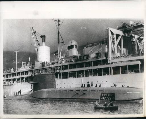 Mar. 03, 1961 - Demonstrators as Polaris Submarines arrives Holy Loch: The 5700 ton American Polaris Submarine Patrick Henry arrived in the Holy Loch, Firth of Clyde today, and tied up alongside the Submarine Depot Ship Proteus . On arrival she was cheered by the Royal Navy and demonstrators in small boats were in evidence on the waters around the vessels. One lone demonstrator in a small canoe, dodged pol~~e launches for some time but eventually he capsized and bad to be fished out of the water by naval frogmen. Photo shows a Demonstrator in a small boat alongside the submarine Patrick Henry, and the depot ship Proteus in the Holy Loch - Forth of Clyde today.  - ZUMAk09