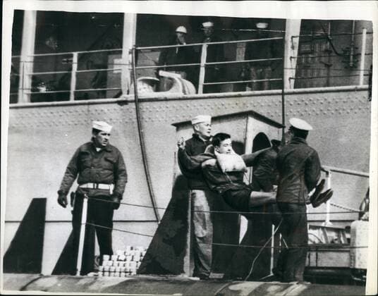 Mar. 03, 1961 - Demonstrator Squa~~ on Nuclear Sub s Tailfin: An anto Polaris demonstrator sat above the waves on the tailfin of America s nuclear submarine Patrick Henry for 45 minutes yesterday in the Holy Loch. He stayed there until he was taken off by the police. He was one of three Commandos who boarded the vessel in defiance of warnings to keep cleat. Two of them were hauled aboard the craft from canoes by sailors and the third sat on the tailfin. Photo shows Sailors carrying one of the demonstrators from the submarine Patrick Henry in the Holy Loch.  - ZUMAk09