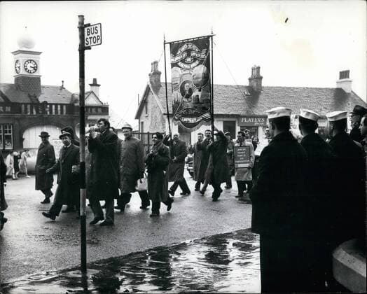 Mar. 03, 1961 - American Sailors Watch Demonstrators In dunoon Submarine Depot Ship Proteus In Holy Loch. Anti-Nuclear campaigners were to be seen in the streets of Dunoon - with their posters - placards etc., - soon after the arrival in the Holy Loch of the American Polaris Submarine Depot ship Proteus .. Photo Shows: Sailors from the Prote~s - watch anti-nuclear campaigners in the streets o Dunoon, Argyll - Fi~th of  - ZUMAk09