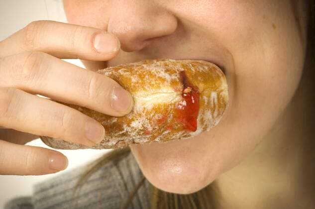 A young female eating a jam donut. Jam donuts have been criticized by junk food activists in the global war on obesity as unhealthy with poor nutritional value. The term ‘junk food’ was coined by Michael Jacobson, director of the Center for Science in the Public Interest, to describe food which contained contain high levels of saturated fat, salt, or sugar and numerous food additives and at the same time is lacking in proteins, vitamins and fibre. Consumption of junk food has been associated with obesity, heart disease, Type 2 diabetes and dental cavities.