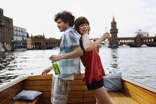 Germany, Berlin, Young couple on motorboat, holding bottles, standing back to back model released property released  VVF00052