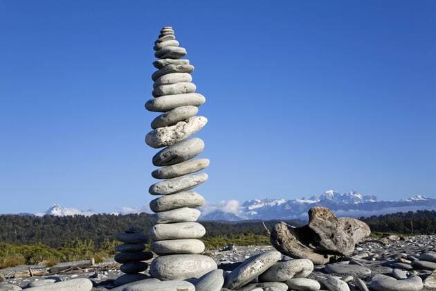 New Zealand, South Island, West Coast, Piles of Stones in beach with mountains in background  GWF001331