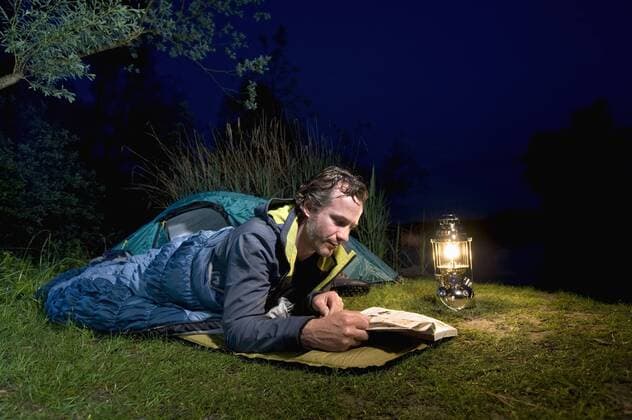 Germany, Bavaria, Ammersee, Man reading book near lakeshore while camping at night model released  RNF000615