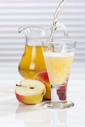 Apple juice being poured into glass besides apples and pitcher  CSF016394