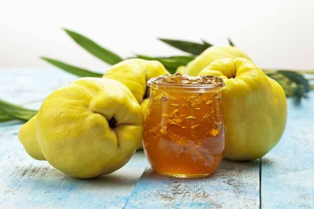 Four quinces (Cydonia oblonga), a spoon and a glass of quince marmalade on wooden table  CSF020323