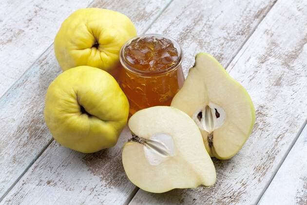 Two and a half quinces (Cydonia oblonga) and a glass of quince marmalade on wooden board  CSF020328