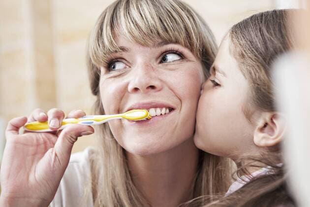 IMAGO Creative: Internationaler Frauentag, Mental Load und Care-Arbeit Germany, North Rhine Westphalia, Cologne, Mother brushing teeth while daughter kissing, close up model released property released  FMKYF000463