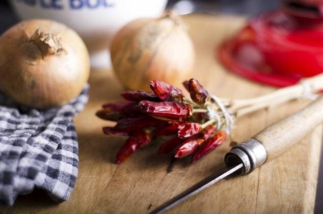 Dried red chili peppers, onions and a knife on wooden chopping board  ODF000679