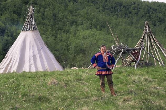 Sami man in traditional clothing, standing in front of lavvu teepee, Lapland, Norway, Europe. 1997.  1072540 PetexOxford