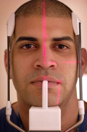 Close up a patient, whose teeth and jaw is being x-rayed by digital radiology which uses red laser beams to align the machine and the patient’s height.