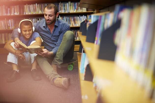 Man reading book to boy with headphones in library model released Symbolfoto property released  ZEF000761