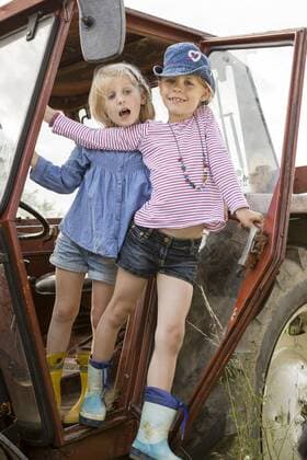 Portrait of two smiling little girls standing on a tractor model released Symbolfoto  FKIF000076