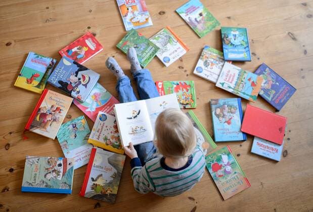 Ein Kind sitzt zwischen vielen Büchern und schaut sich ein Buch an, aufgenommen am 28.01.2015.