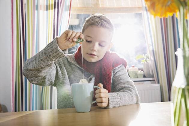 Boy having a cold sitting in the kitchen with cup of tea model released Symbolfoto property released  PDF000760