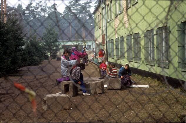 Reportage Flüchtlingslager in Hinrichshagen bei Rostock 1993, Flüchtlinge hinter einem mit Stacheldraht versehenem Maschendrahtzaun