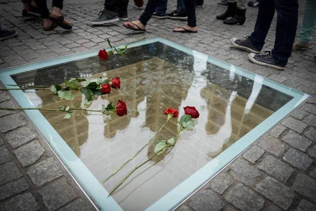 Rote Rosen liegen auf der neuen Scheibe fürs Mahnmal zur Bücherverbrennung am Berliner Bebelplatz, in ihr spiegeln sich die jungen Touristen, während sie die darunter befindlichen leeren Bücherregale betrachten.