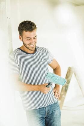 Smiling young man renovating holding paint roller model released Symbolfoto  UUF004161