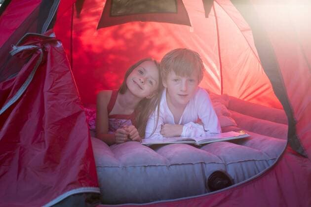 Portrait of brother and sister lying in a red tent with a book model released Symbolfoto  SARF001931