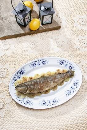 Fish plate in greek tavern. Roasted trout on onion. Fresh salads in the background, pretty beige handmade table cloth. Decorative lanterns and lemons.  Copyright: KantarukxAgnieszka bew180F5AD