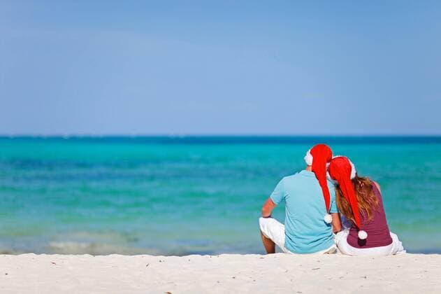 ein verliebtes Paar sitzt mit Nikolausmuetzen am Sandstrand a couple in love sitting with Santa hats at sandy beach BLWS269804