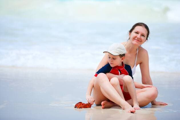 eine junge Mutter sitzt mit ihrem kleinen Sohn am Strand und blickt in die Kamera a young mother sitting with her son at the beach and looking to the camera BLWS269839