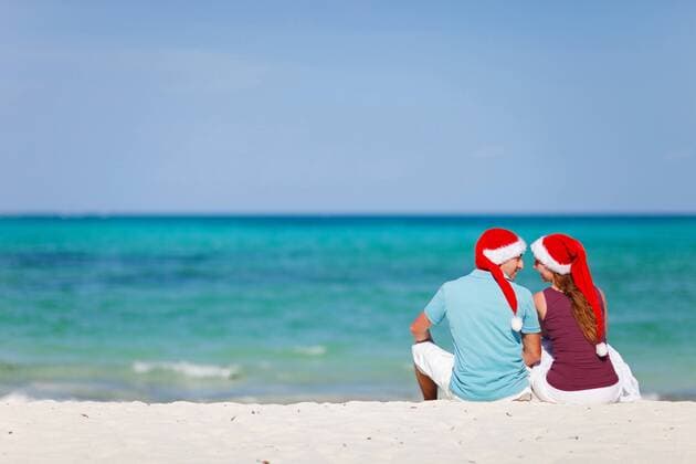 ein verliebtes Paar sitzt mit Nikolausmuetzen am Sandstrand a couple in love sitting with Santa hats at sandy beach BLWS269803