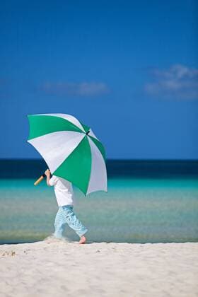 kleiner Junge mit grossem Sonnenschirm am Sandstrand little boy with sunshade walking on sandy beach BLWS269822