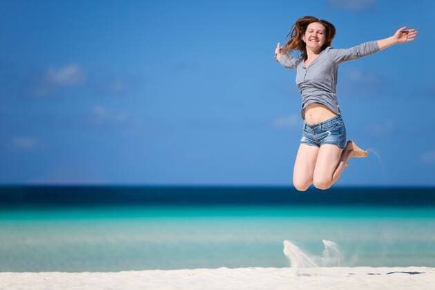 junge Frau macht einen Luftsprung am Sandstrand young woman jumping with joy on sandy beach BLWS269823