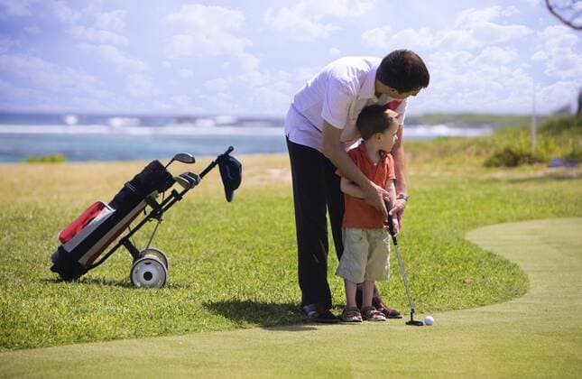 Vater zeigt seinem Sohn das Golfspielen auf einem Golfplatz Father teaching his sun playing golf on a golf course BLWS234330