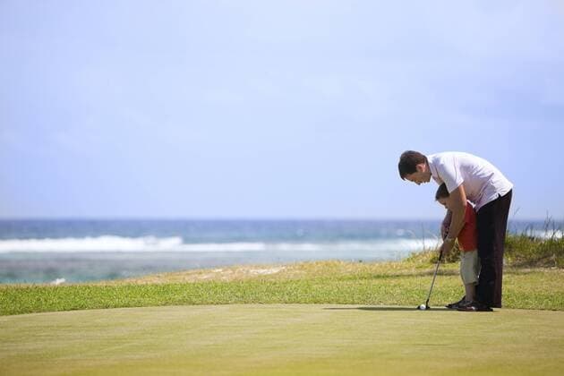 Vater zeigt seinem Sohn das Golfspielen auf einem Golfplatz am Meer Father teaching his sun to play golf on a golf course BLWS234331