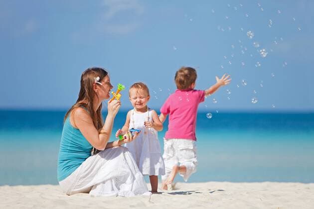 Mutter sitzt mit ihren Kindern am Strand und macht Seifenblasen mother sitting with her two children on the beach and blowing bubbles BLWS269826