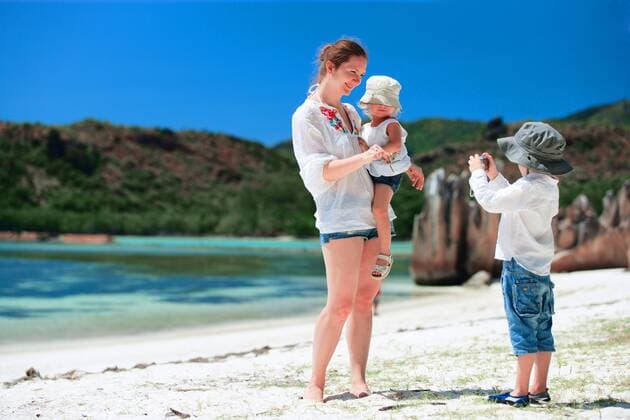 ein kleiner Junge fotografiert seine Mutter mit seiner Schwester an einem tropischen Strand a little boy taking a photo from his mother and his sister on tropical beach BLWS269844