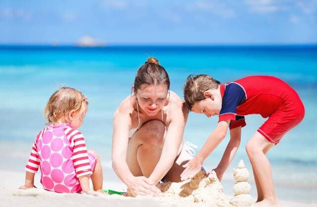 eine junge Mutter baut mit ihren zwei kleinen Kindern eine Sandburg am Strand a young mother and her two children building a sand castle on sandy beach BLWS270807
