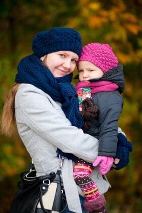 Mutter haelt ihre kleine Tochter auf dem Arm, beide in warmer Kleidung mit Strickmuetze und Schal mother cradling her daughter, both in warm clothing with woolen hat and scarf BLWS272475
