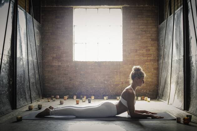 A blonde woman, in a white crop top and leggings,lying on a yoga mat on the floor surrounded by candles, doing yoga. A blonde woman, in a white crop top and leggings,lying on a yoga mat on the floor surrounded by candles, doing yoga.  16687