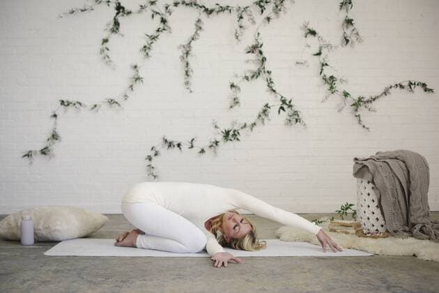 A blonde woman, in a white leotard and leggings, kneeling on a yoga mat with her arms stretched forwards. A blonde woman, in a white leotard and leggings, kneeling on a yoga mat with her arms stretched forwards.  16706