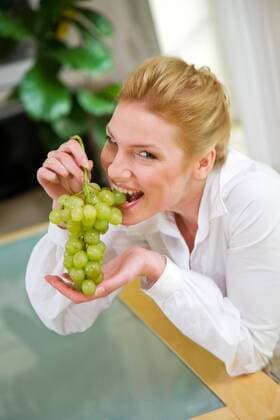 Woman eating grapes, sitting next to the table.  1272426