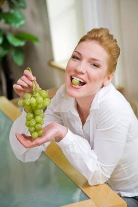 Woman eating grapes, sitting next to the table.  1272427