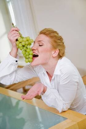 Woman eating grapes, sitting next to the table.  1272430