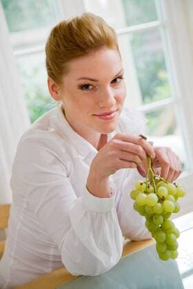 Woman eating grapes, sitting next to the table.  1272432