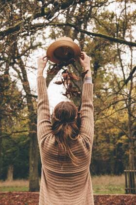 Back view of young woman dropping dried leaves on her head from a hat at park model released Symbolfoto  CHAF000208
