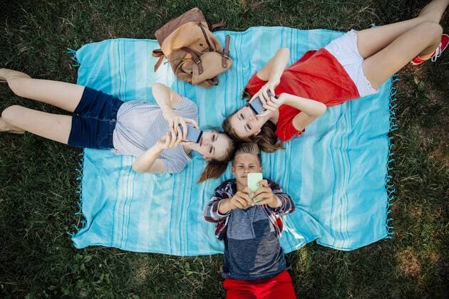 Three teenage friends with smartphones lying on blanket model released Symbolfoto  AIF000066