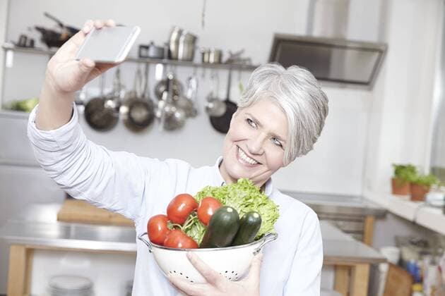 Mature woman holding colander with vegetables taking selfie model released Symbolfoto property released  FMKF002080
