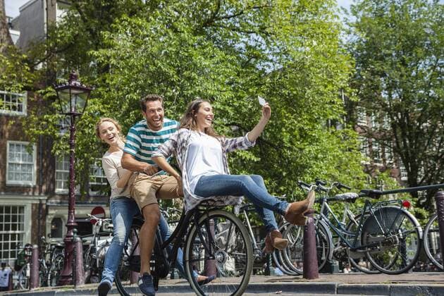 Netherlands, Amsterdam, three playful friends riding on one bicycle in the city model released Symbolfoto  FMKF002146