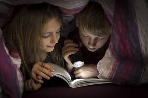 IMAGO Creative: Jahreszeit Winter, Fantasievoll drinnen spielen Brother and sister reading book under a blanket  SARF002302