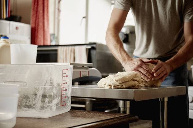 A man, a baker working in a commercial kitchen kneading a large piece of dough. A man, a baker working in a commercial kitchen kneading a large piece of dough.  18443